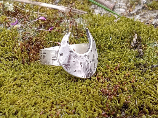 Silver ring with a crescent moon that has a big belly and hammered texturing, ring is on a mossy surface