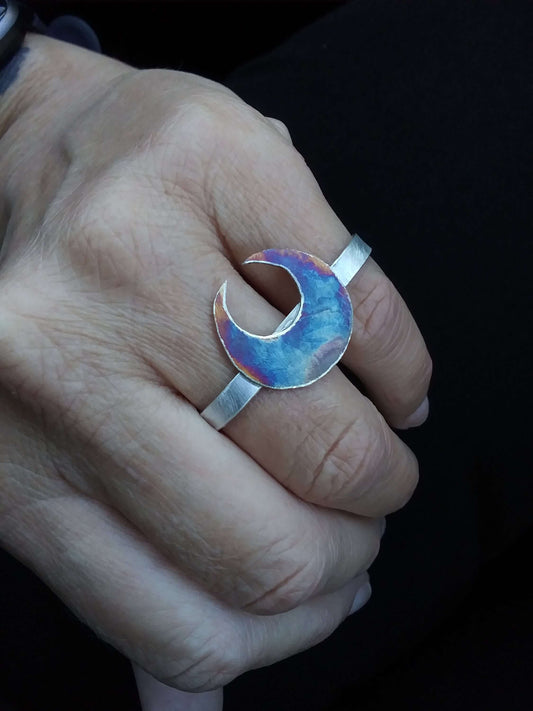 A silver double ring with a crescent moon that has unique patina worn between the ring and pinky finger of a model.