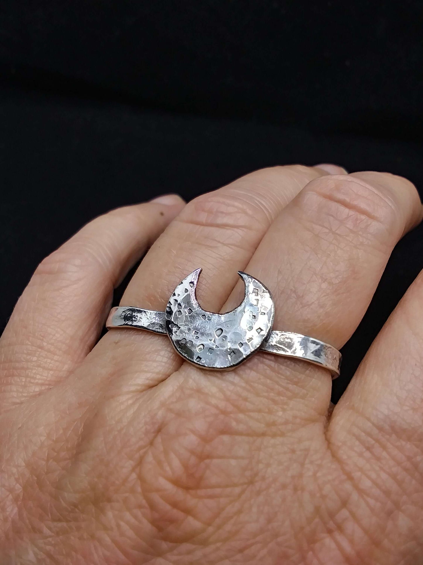 Top view of a silver double ring with a crescent moon that has hammered texturing on a hand with folded fingers.