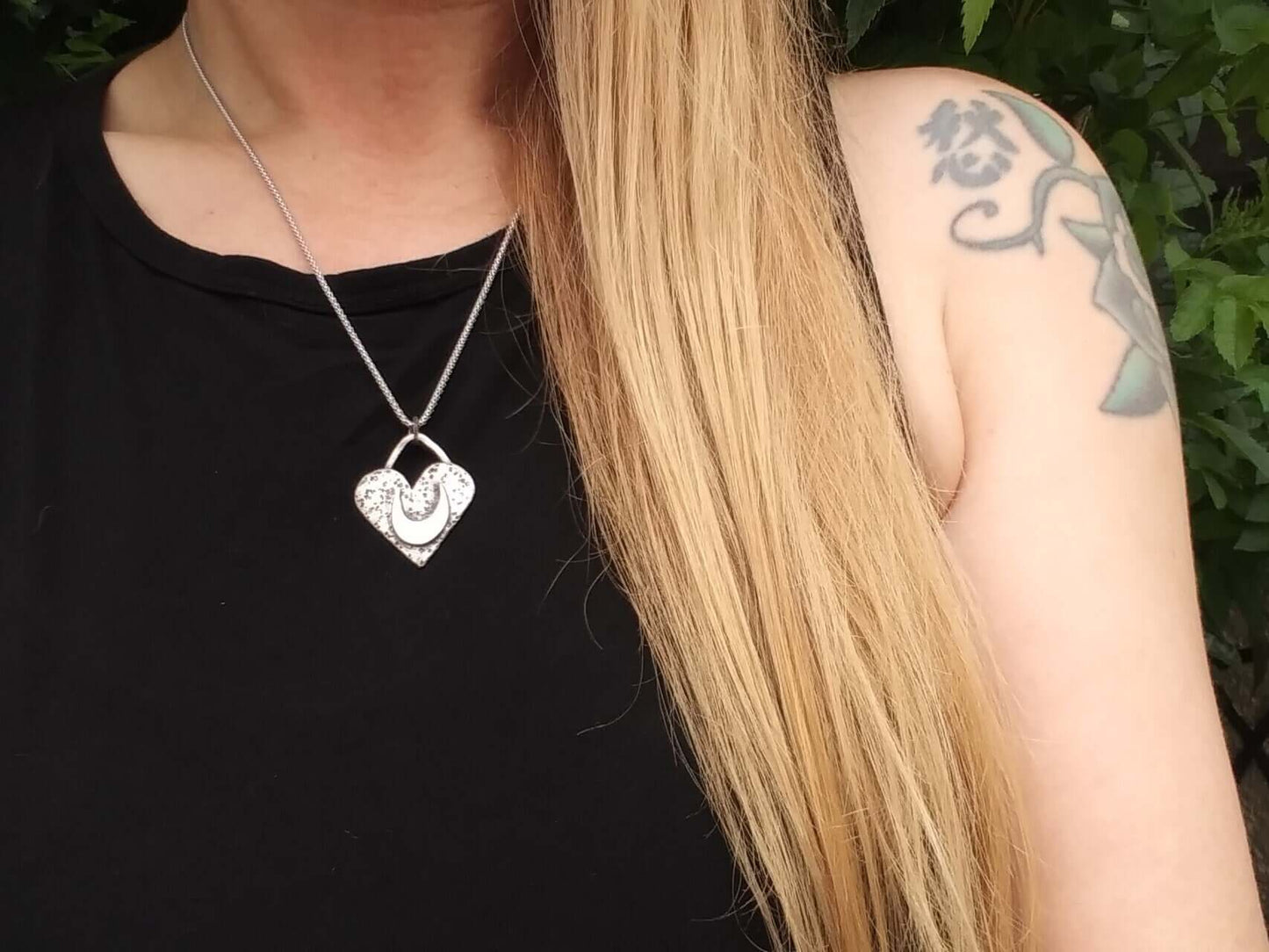 Silver heart charm worn by blonde model in sleeveless black top with tattoos