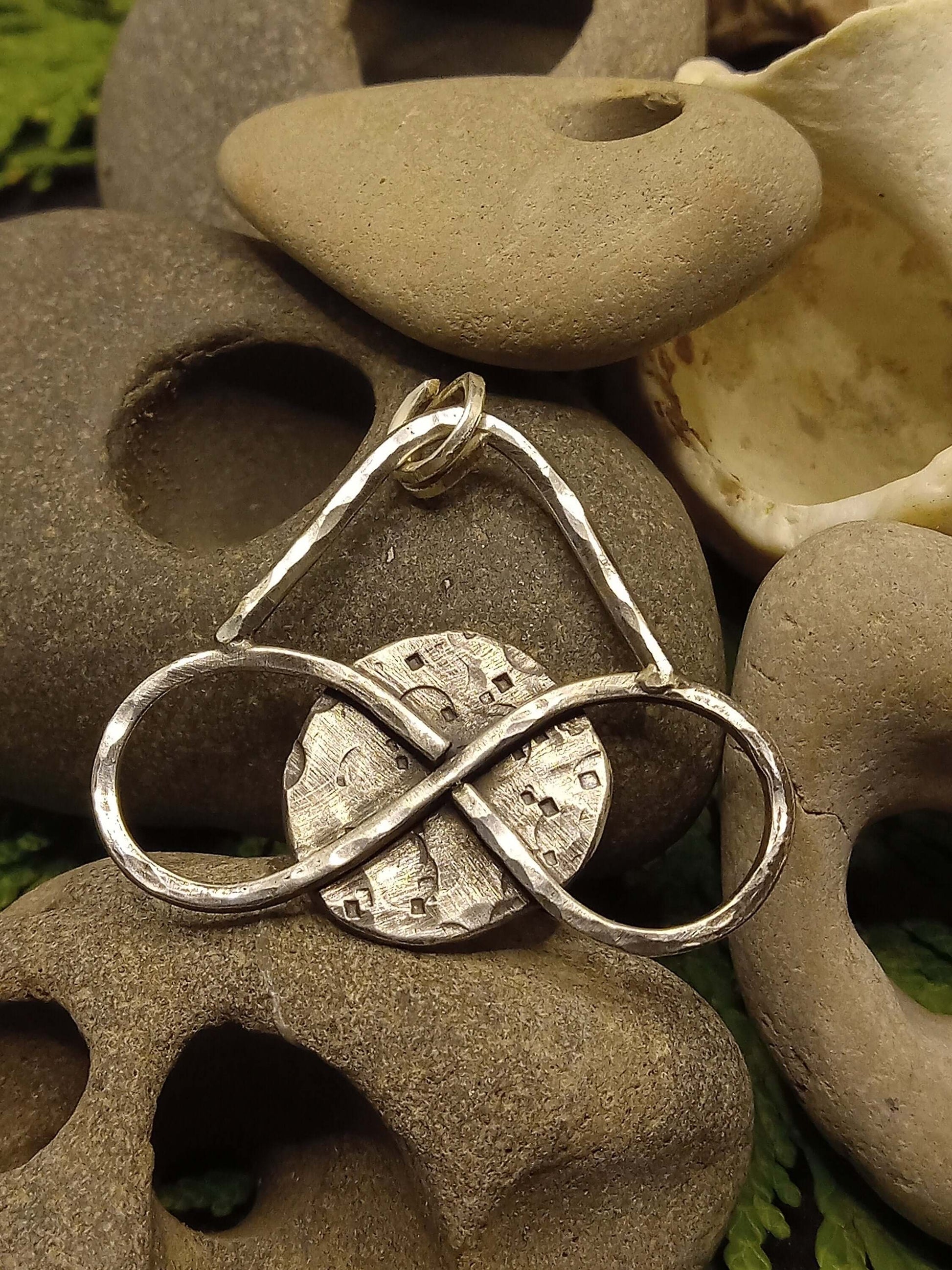  Medium sized silver pendant with dark patina that depicts a horizontal eternity symbol inlaid over a full moon rested on hagstones.