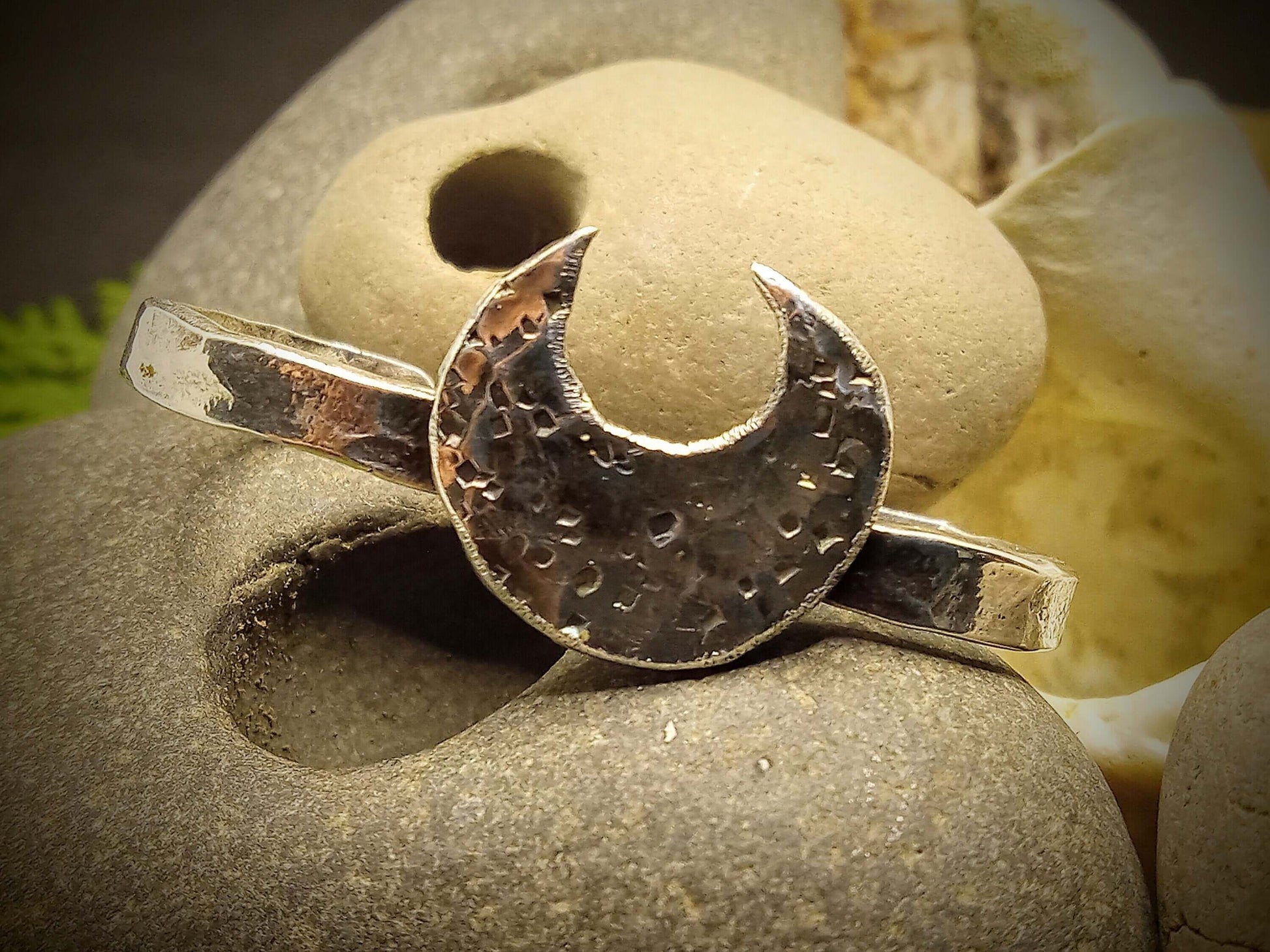 A silver double ring with a crescent moon that has hammered texturing rested next to a hagstone.